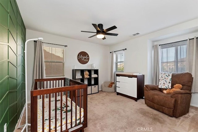 carpeted bedroom featuring ceiling fan and a crib