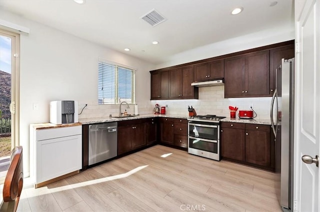 kitchen featuring sink, light stone counters, light hardwood / wood-style flooring, stainless steel appliances, and backsplash