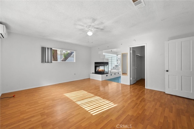 unfurnished living room with a textured ceiling, a wall unit AC, ceiling fan, light hardwood / wood-style flooring, and a multi sided fireplace