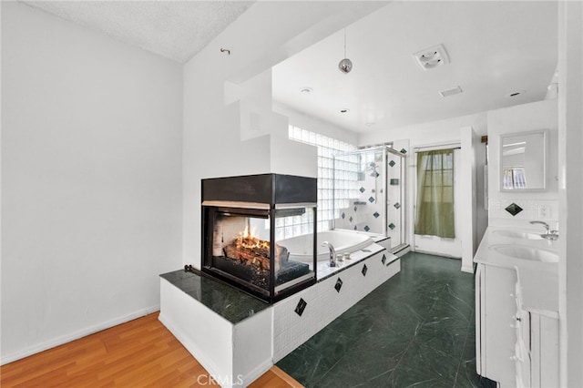 bathroom with hardwood / wood-style floors, vanity, a multi sided fireplace, and shower with separate bathtub