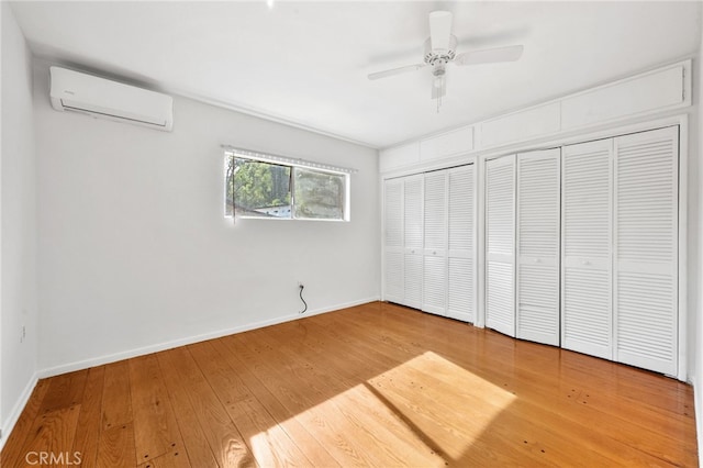 unfurnished bedroom featuring an AC wall unit, ceiling fan, two closets, and hardwood / wood-style flooring