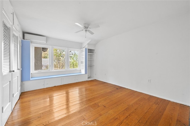 spare room featuring ceiling fan, light wood-type flooring, and a wall unit AC