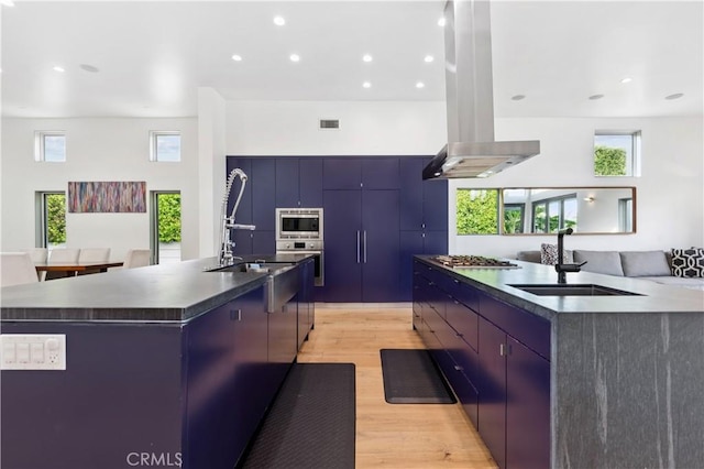 kitchen featuring island exhaust hood, stainless steel appliances, a spacious island, sink, and light hardwood / wood-style floors