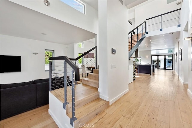 stairs with wood-type flooring, a towering ceiling, and plenty of natural light