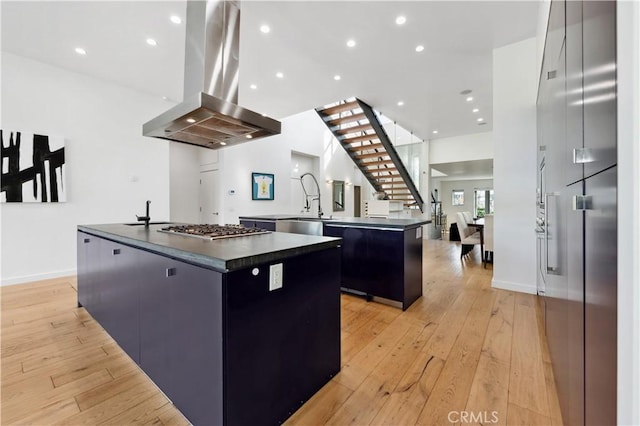 kitchen featuring light wood-type flooring, a large island, island range hood, kitchen peninsula, and stainless steel gas cooktop