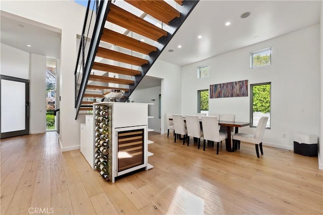 dining area featuring a high ceiling, light wood-type flooring, and beverage cooler