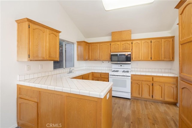 kitchen with kitchen peninsula, light wood-type flooring, white range oven, sink, and tile counters