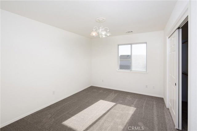 unfurnished room featuring dark carpet and an inviting chandelier