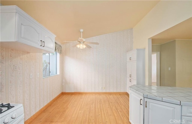 kitchen with light hardwood / wood-style flooring, ceiling fan, tile counters, white range oven, and white cabinetry