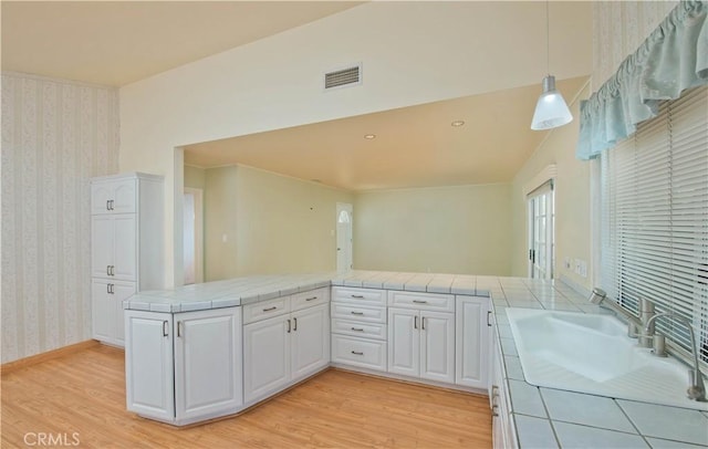 kitchen with kitchen peninsula, tile countertops, light hardwood / wood-style flooring, white cabinets, and hanging light fixtures