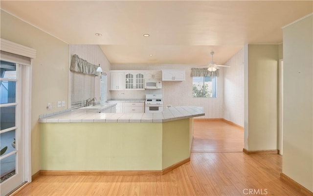 kitchen with white appliances, white cabinets, light hardwood / wood-style flooring, tile counters, and kitchen peninsula