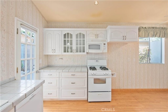 kitchen with white cabinets, white appliances, light hardwood / wood-style flooring, and tile counters