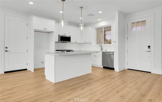 kitchen featuring a kitchen island, appliances with stainless steel finishes, decorative light fixtures, white cabinets, and light hardwood / wood-style flooring