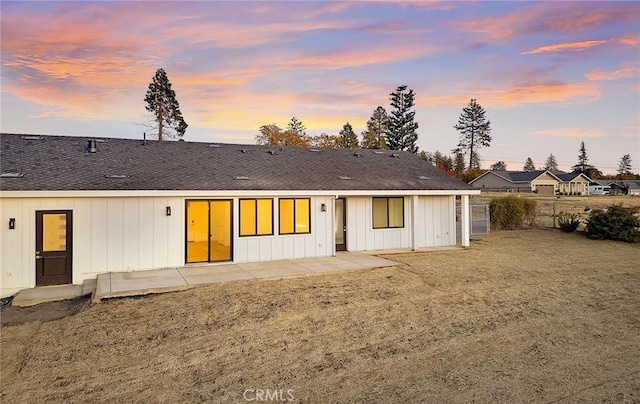 back house at dusk with a lawn and a patio