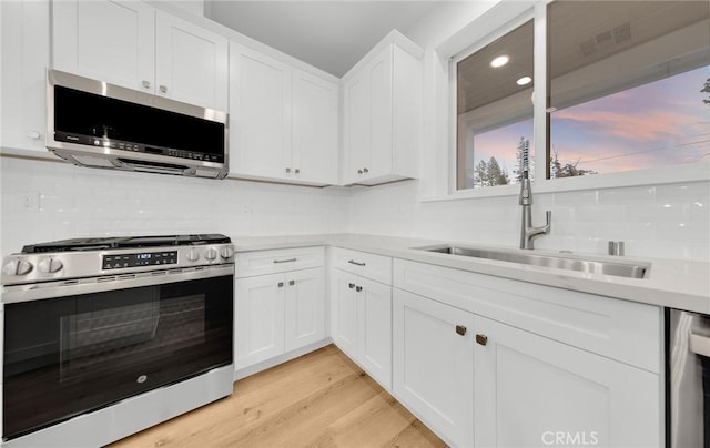 kitchen with white cabinetry, sink, stainless steel appliances, and light hardwood / wood-style floors