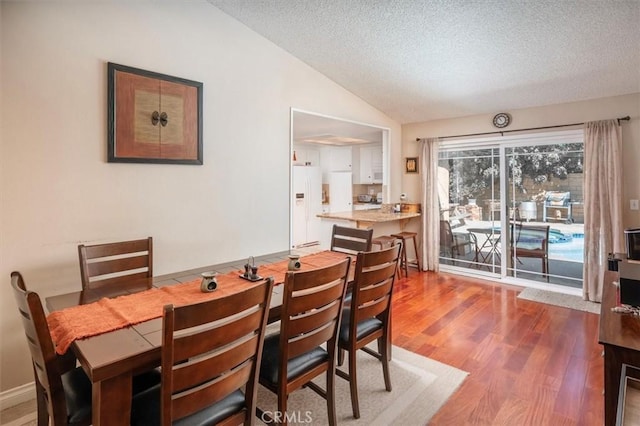 dining room with a textured ceiling, vaulted ceiling, and hardwood / wood-style flooring