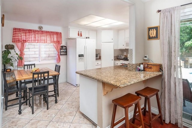 kitchen featuring white refrigerator with ice dispenser, white cabinets, tasteful backsplash, light tile patterned flooring, and kitchen peninsula