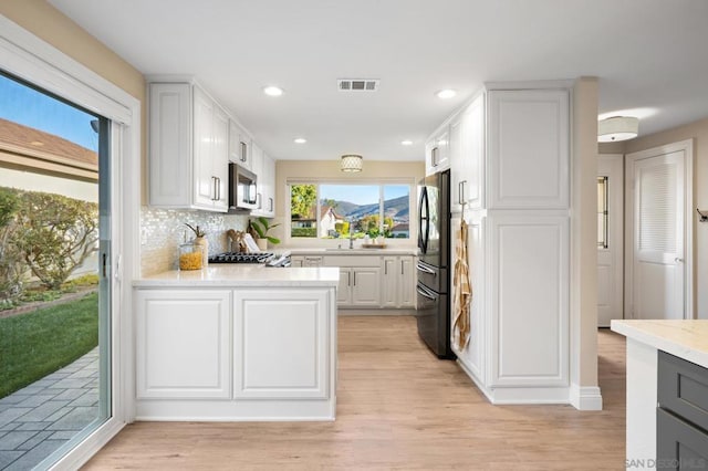 kitchen featuring white cabinetry, sink, backsplash, light hardwood / wood-style floors, and appliances with stainless steel finishes