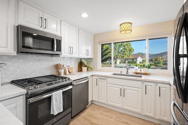 kitchen with sink, appliances with stainless steel finishes, white cabinetry, light stone countertops, and decorative backsplash