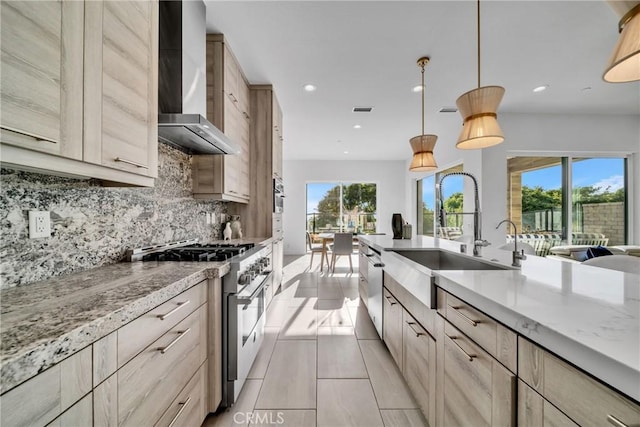 kitchen with light brown cabinets, wall chimney exhaust hood, stainless steel appliances, and decorative light fixtures