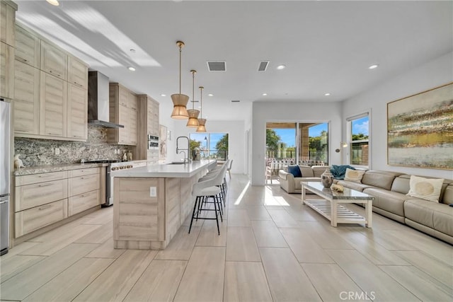 kitchen with pendant lighting, a kitchen island with sink, wall chimney exhaust hood, a breakfast bar area, and stainless steel range with gas stovetop