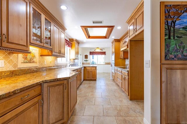 kitchen with sink, ceiling fan, decorative backsplash, light stone countertops, and kitchen peninsula