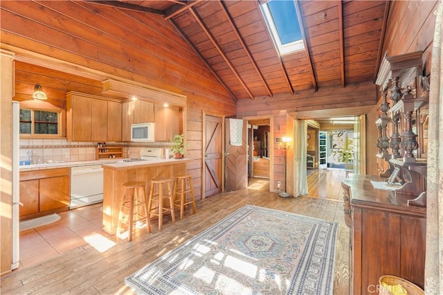 kitchen with white appliances, light hardwood / wood-style flooring, a breakfast bar, kitchen peninsula, and wooden walls