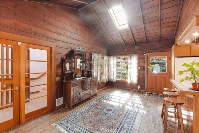 foyer entrance with vaulted ceiling with skylight, french doors, wood ceiling, wood walls, and light wood-type flooring