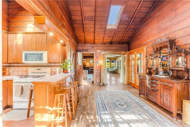 kitchen with white appliances, a kitchen breakfast bar, vaulted ceiling with skylight, tile counters, and wood ceiling