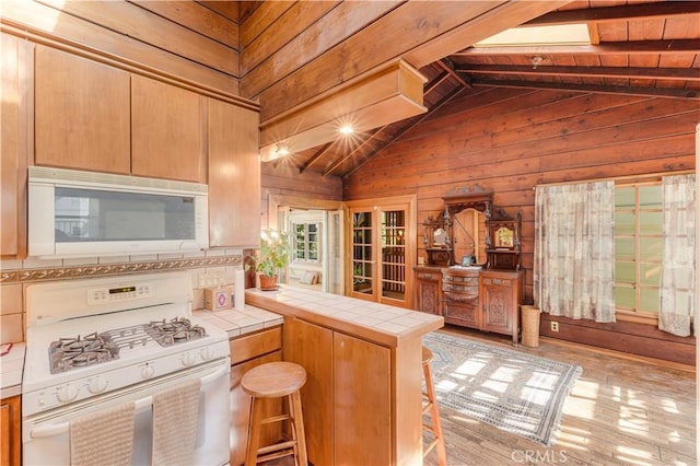 kitchen featuring white appliances, lofted ceiling with beams, kitchen peninsula, tile counters, and a breakfast bar area