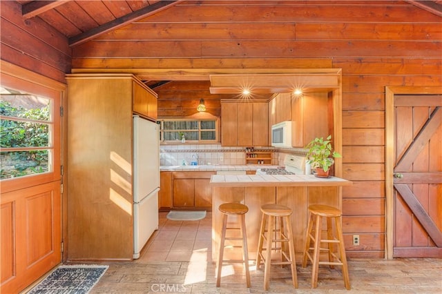 kitchen with tile countertops, a breakfast bar, white appliances, tasteful backsplash, and lofted ceiling with beams