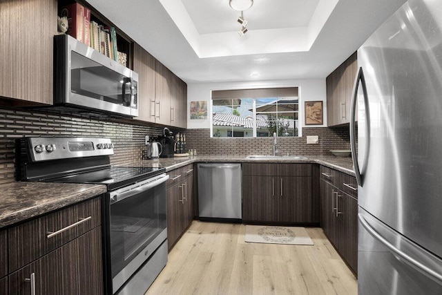 kitchen featuring backsplash, light wood-type flooring, stainless steel appliances, a raised ceiling, and sink