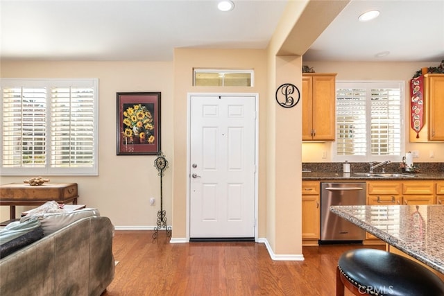 interior space with dark stone countertops, dark hardwood / wood-style flooring, stainless steel dishwasher, and sink