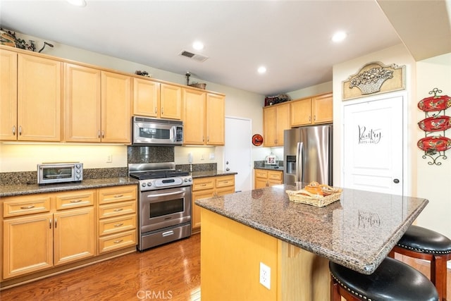 kitchen featuring a center island, dark wood-type flooring, dark stone counters, appliances with stainless steel finishes, and a breakfast bar area