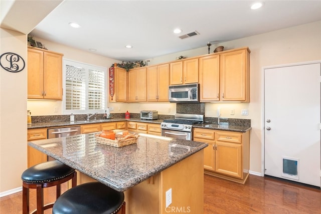 kitchen with dark stone countertops, a center island, stainless steel appliances, and hardwood / wood-style flooring