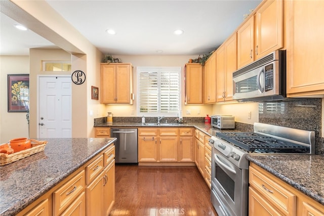 kitchen featuring dark hardwood / wood-style flooring, stainless steel appliances, dark stone counters, and sink