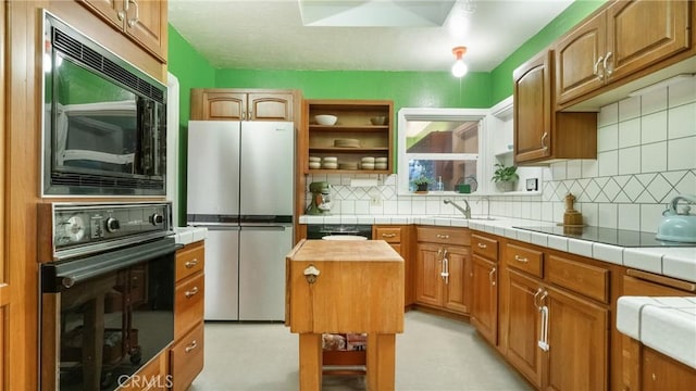 kitchen with black appliances, tile counters, sink, and backsplash