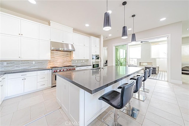 kitchen with a center island with sink, sink, appliances with stainless steel finishes, decorative light fixtures, and a kitchen bar