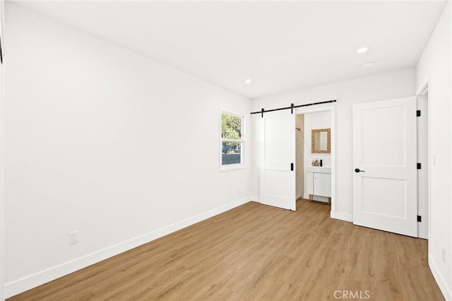 unfurnished bedroom with light hardwood / wood-style floors and a barn door