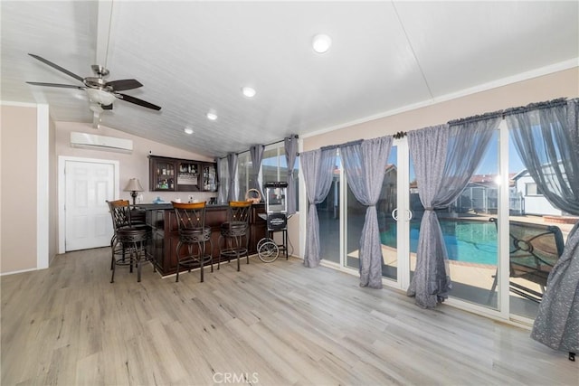 interior space with ceiling fan, a wall unit AC, light hardwood / wood-style floors, lofted ceiling, and a breakfast bar