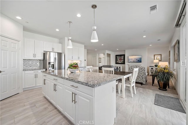 kitchen with hanging light fixtures, stainless steel refrigerator with ice dispenser, a kitchen island, and white cabinets