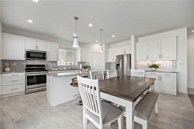 kitchen featuring a kitchen island, white cabinetry, hanging light fixtures, stainless steel appliances, and light stone countertops