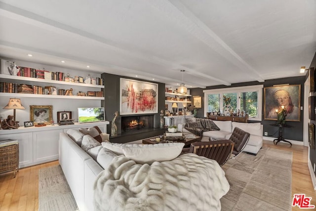 living room with beam ceiling, built in shelves, and light hardwood / wood-style floors