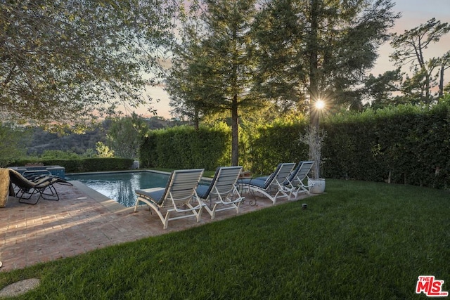 pool at dusk with a patio area and a yard