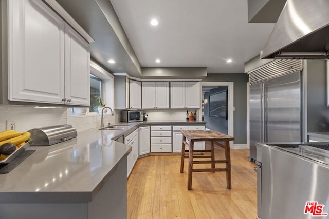 kitchen with backsplash, light wood-type flooring, sink, white cabinetry, and range hood