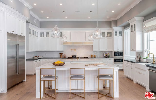 kitchen with a center island with sink, sink, light hardwood / wood-style flooring, built in appliances, and decorative light fixtures