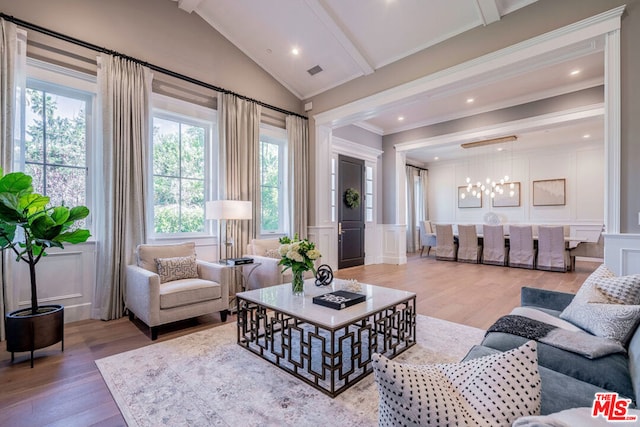 living room with vaulted ceiling with beams, wood-type flooring, ornamental molding, and a chandelier