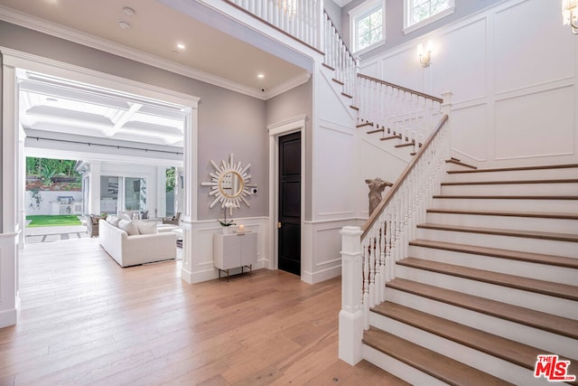 foyer featuring coffered ceiling, ornamental molding, a wealth of natural light, and light hardwood / wood-style flooring