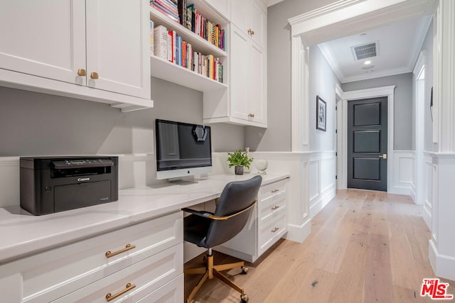 office space featuring light wood-type flooring, built in desk, and ornamental molding