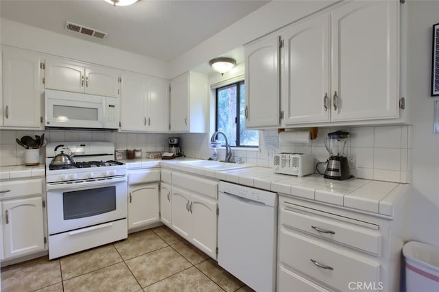 kitchen featuring tile countertops, white appliances, sink, tasteful backsplash, and white cabinetry